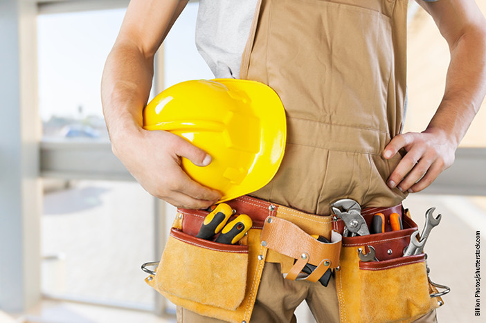 Handwerker mit gelbem Schutzhelm und Werkzeuggürtel, bereit für den Einsatz auf der Baustelle.