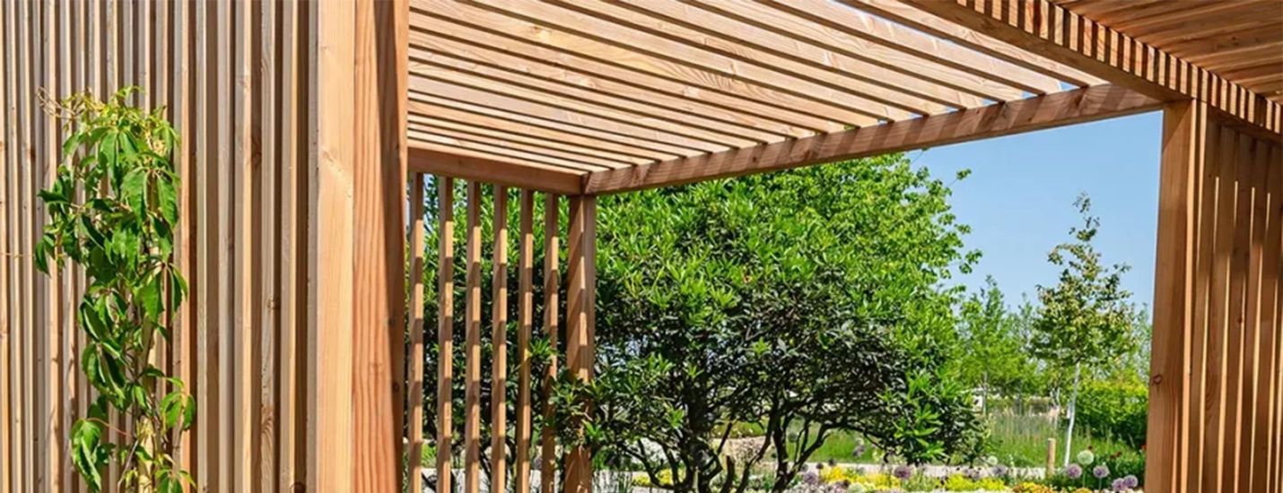 Pergola aus Holz mit Lamellendach und seitlicher Holzverkleidung – sonniger Gartenbereich mit Blick ins Grüne.